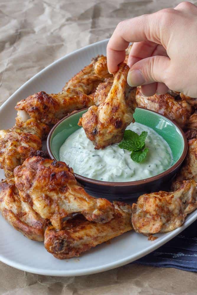 platter of chicken wings with hand dipping a chicken wing into raita sauce