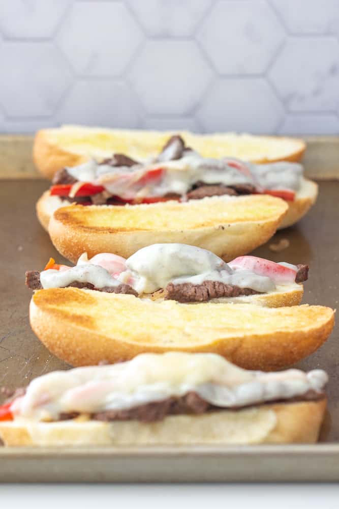 open steak and cheese sandwiches on a baking sheet for broiling