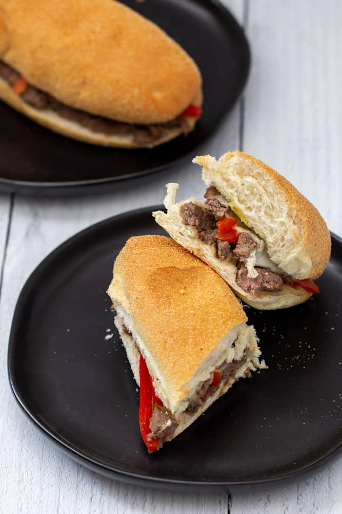sliced steak and cheese sandwiches on black plates, overhead view
