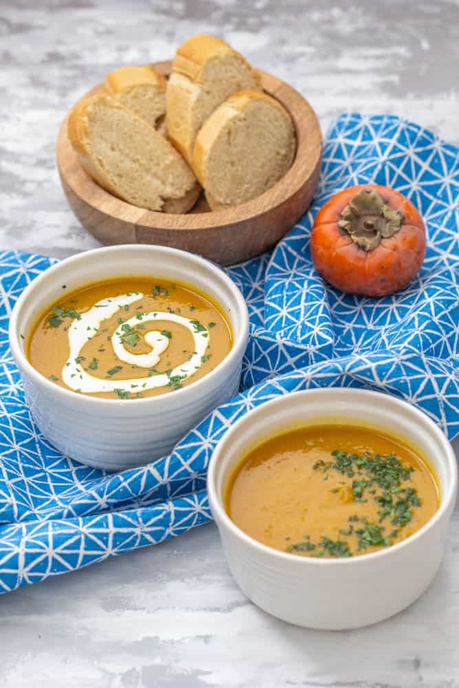 persimmon soup in two bowls with a bowl of bread