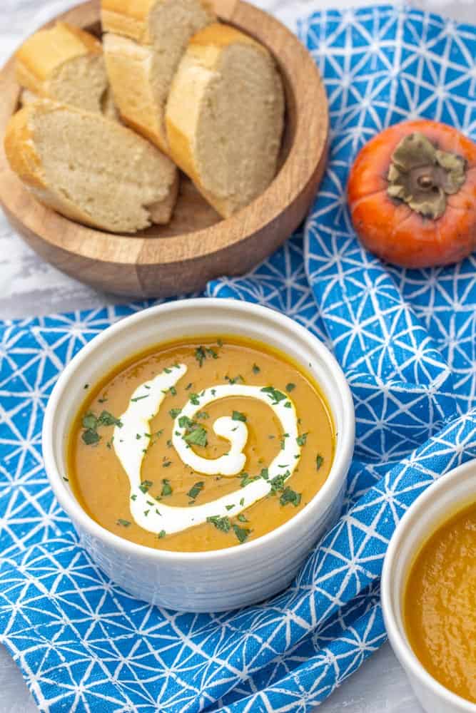 persimmon soup in a bowl with a swirl of creme and chopped parsley