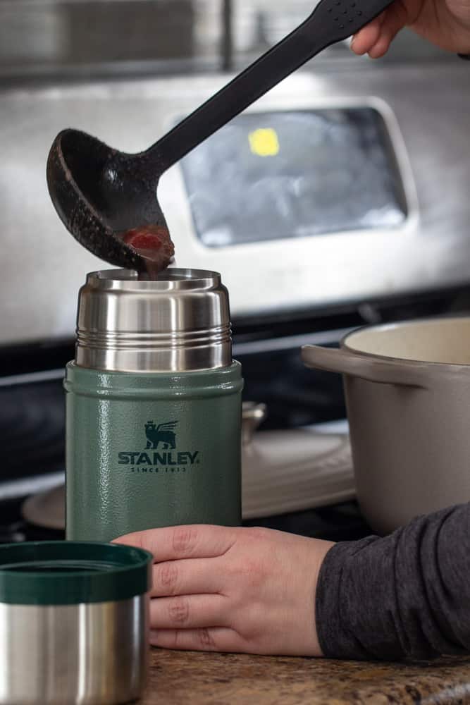 ladle pouring soup into green Stanley food jar on a kitchen counter