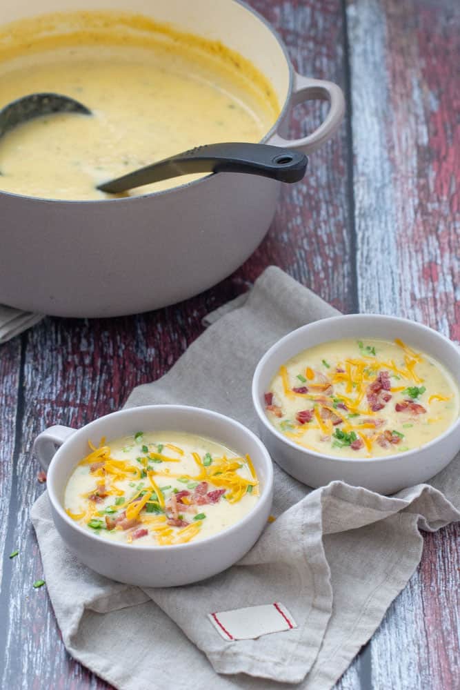 baked potato soup in two shallow bowls with dutch oven behind