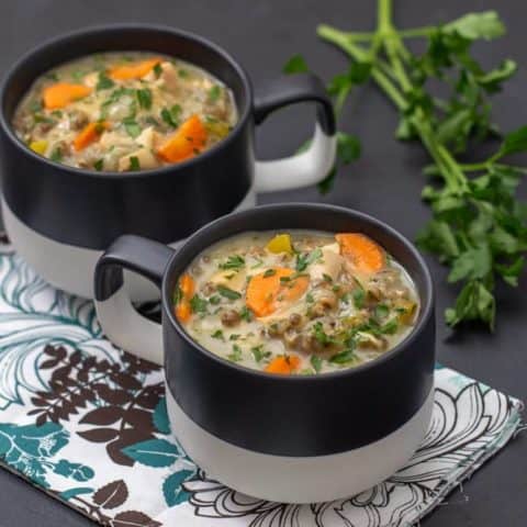 chicken wild rice soup in black and white mugs with a floral napkin on a black countertop