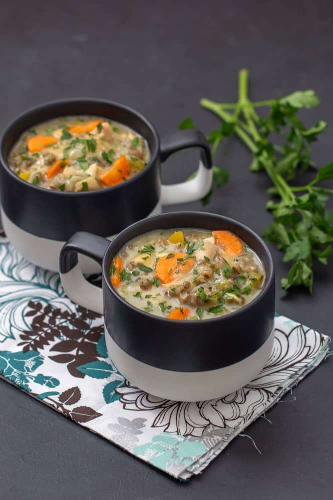 chicken wild rice soup in black and white mugs with a floral napkin on a black countertop