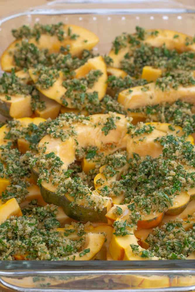 uncooked winter squash in a casserole dish with herb topping
