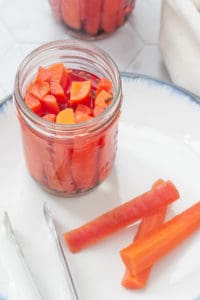 pickled carrots in a jar with carrots and tongs on a plate