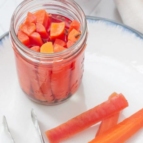 pickled carrots in a jar with carrots and tongs on a plate