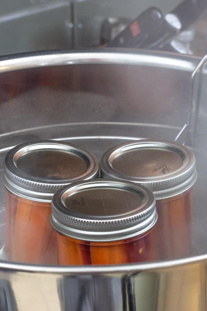filled jars of pickled carrots resting in a canning pot
