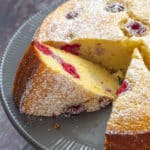 close up of sliced ricotta cake with raspberries and lemon on a gray cake plate