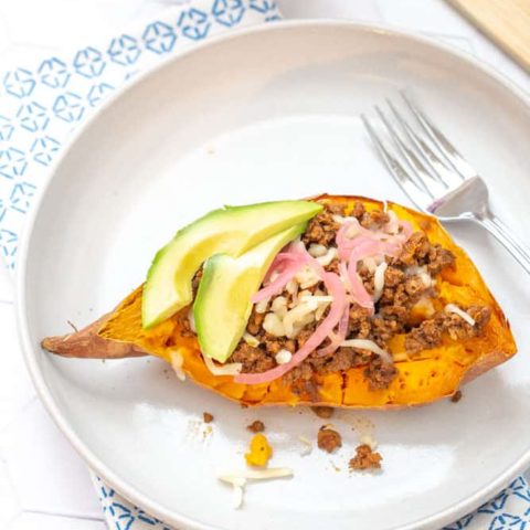 overhead of sweet potato topped with meat, cheese and other toppings on a plate with a decorative napkin