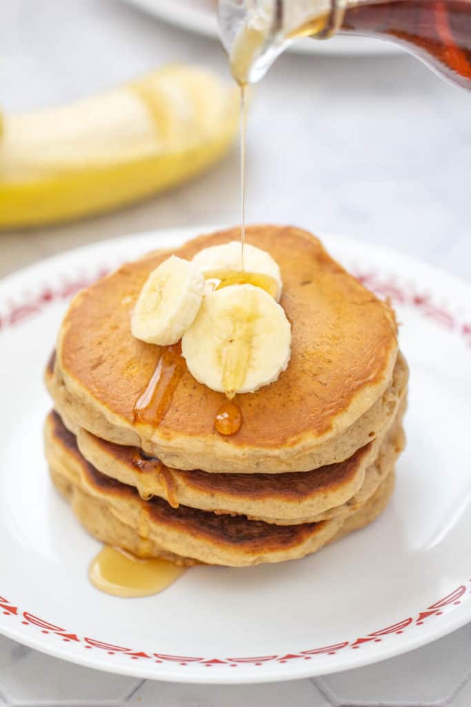 syrup being poured onto banana bread pancakes