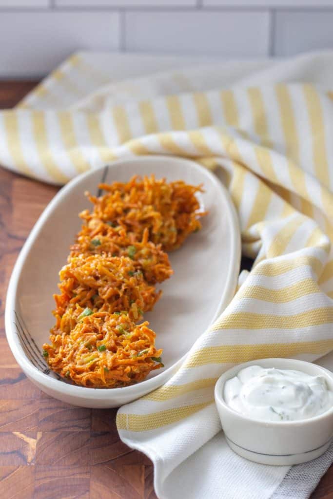 carrot fritters on a white plate with a yellow napkin and a white bowl of dill sauce