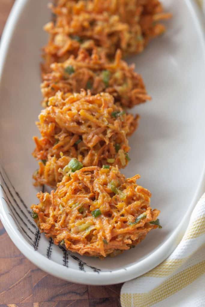 carrot fritters in a row on a white serving platter