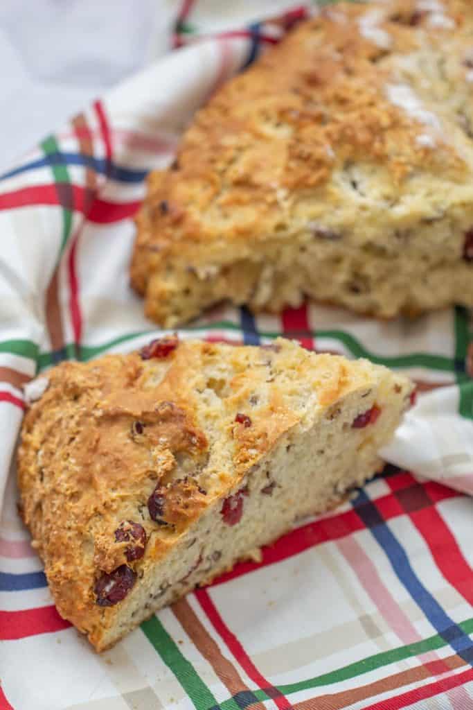 slice of cranberry soda bread with pecans on a plaid kitchen towel