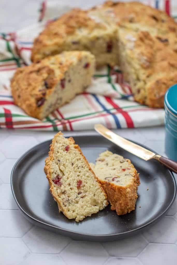 sliced cranberry soda bread on a black plate with loaf behind