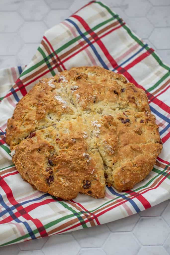 loaf of cranberry soda bread with pecans on a plaid kitchen towel