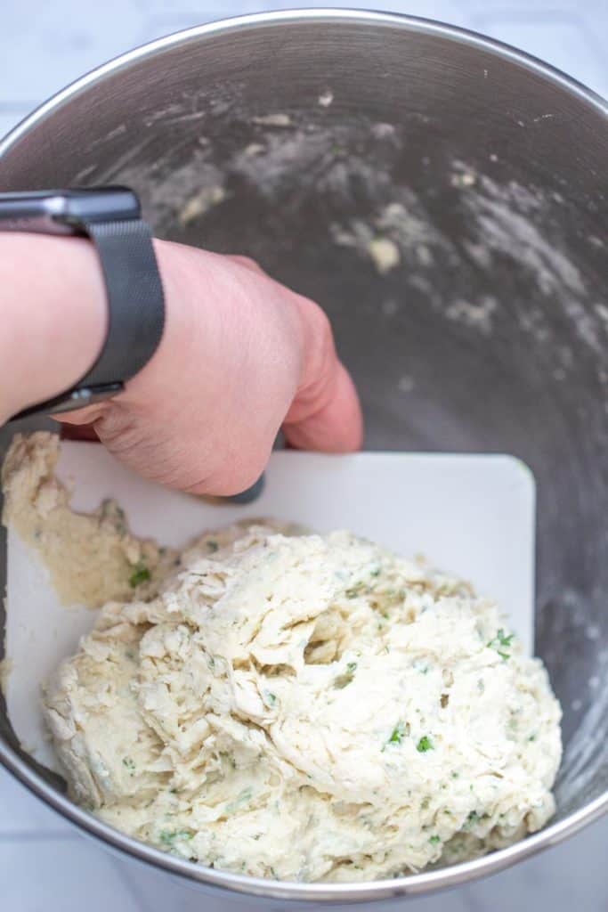 hand mixing herb pizza dough in metal bowl