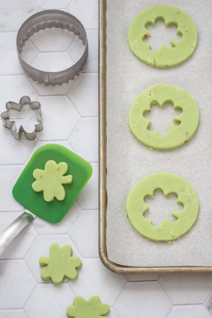 unbaked pistachio pudding cookies on a tray with spatula and cookie cutters