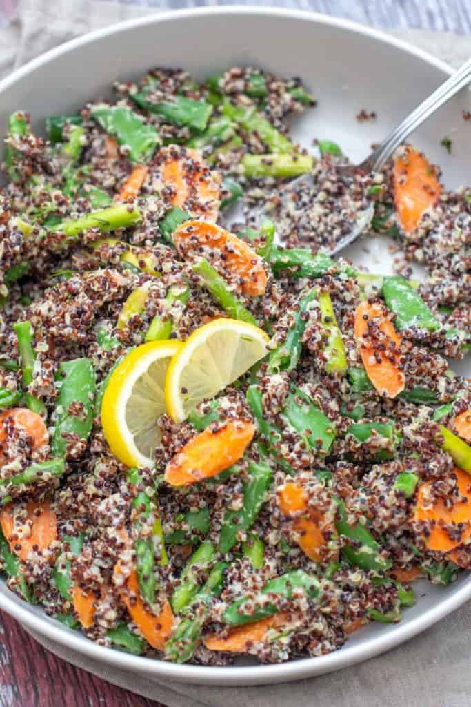 quinoa primavera with carrots, peas, and asparagus in a gray serving dish with a spoon