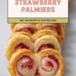 Close-up of strawberry palmiers with jalapeño, flaky puff pastry cookies featuring a sweet and spicy strawberry filling, arranged in a row on a plate. Text overlay reads "Strawberry Palmiers.