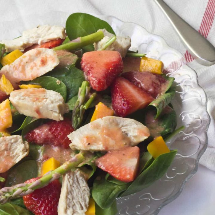 close up of a salad with chicken, fruit, and citrus dressing on a glass plate