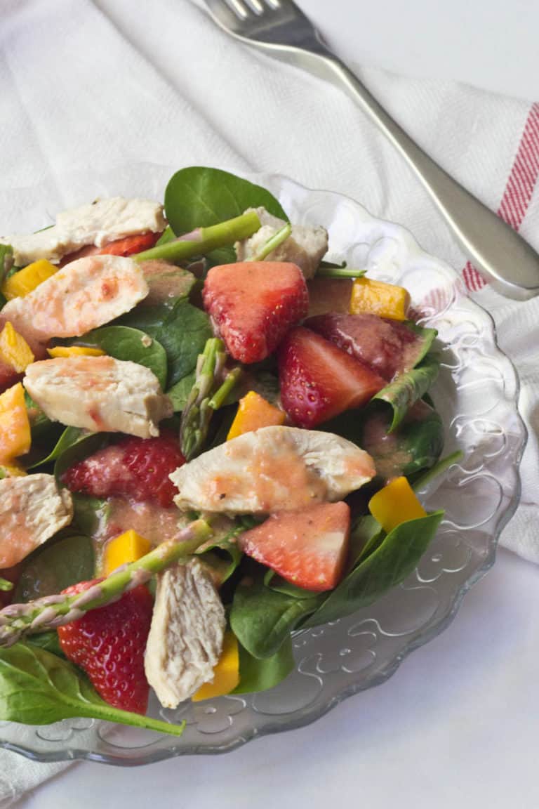 close up of a salad with chicken, fruit, and citrus dressing on a glass plate