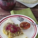 red-rimmed white plate with taco meatloaf on a tortilla with salsa and pickled onions