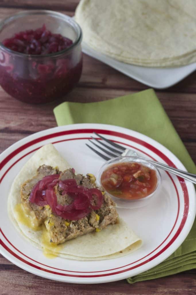 red-rimmed white plate with taco meatloaf on a tortilla with salsa and pickled onions