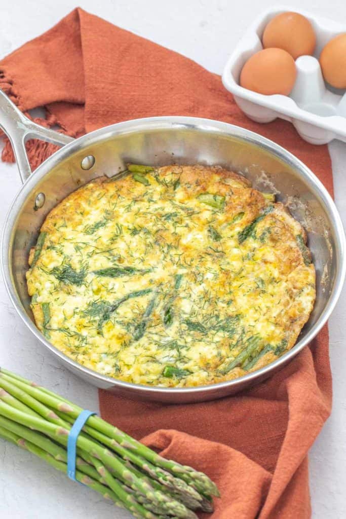 asparagus dill frittata in saute pan with orange napkin underneath