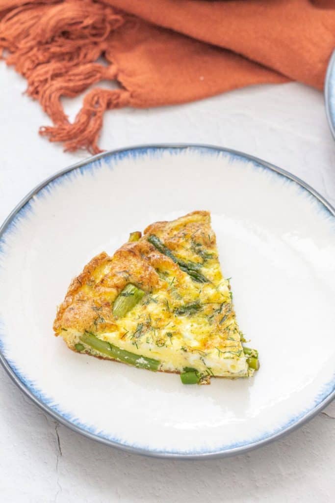 slice of asparagus dill frittata on a white plate with blue rim