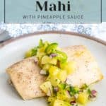 A serving of baked mahi mahi topped with pineapple sauce, garnished with green peppers and red onions, on a white plate. A small dollop of strawberry vanilla jam adds a touch of sweetness. "Baked Mahi Mahi with Pineapple Sauce" text is displayed above the dish.