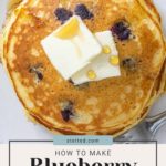 Stack of blueberry pancakes topped with butter and syrup, with a dollop of strawberry vanilla jam on the side. "How to Make Blueberry Pancakes" text overlay on bottom.