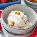 A scoop of strawberry pretzel ice cream with crunchy pretzel pieces is served in a gray bowl, set atop a red and white striped cloth.