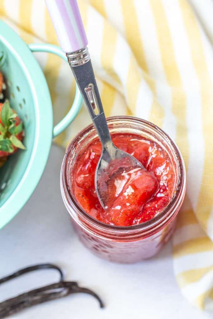 overhead of strawberry vanilla jam in a jar with a spoon scooping