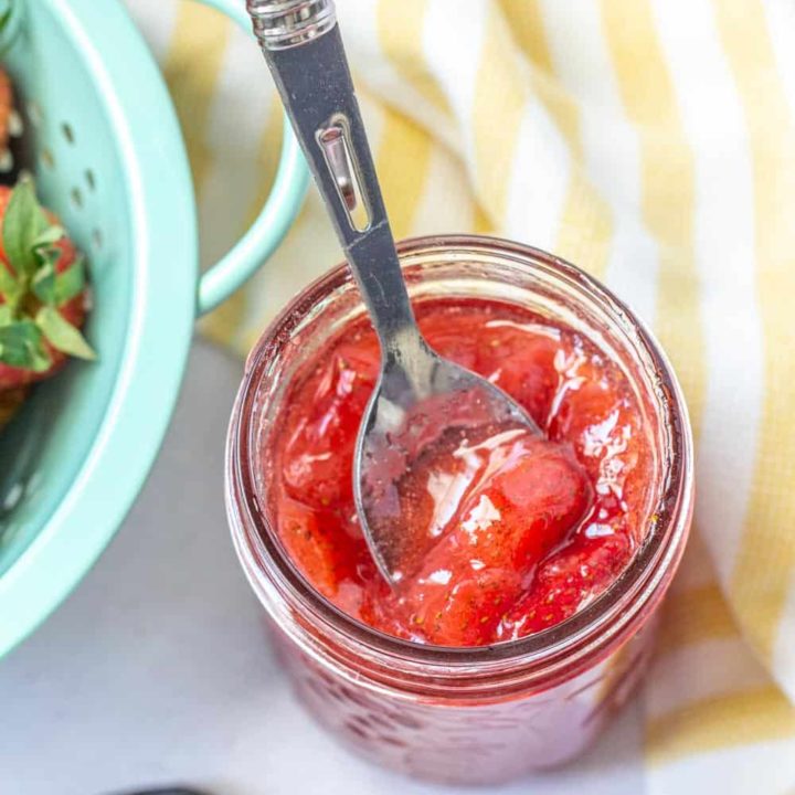 overhead of strawberry vanilla jam in a jar with a spoon scooping