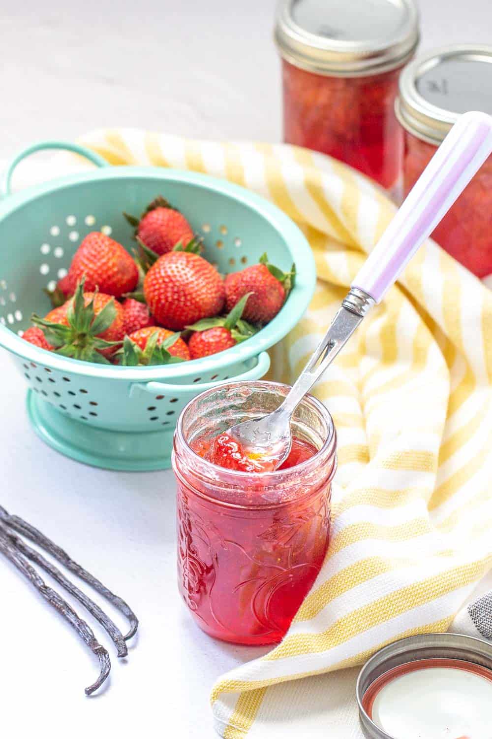 strawberry vanilla jam in a jar and vanilla beans, strawberries and jars on a table