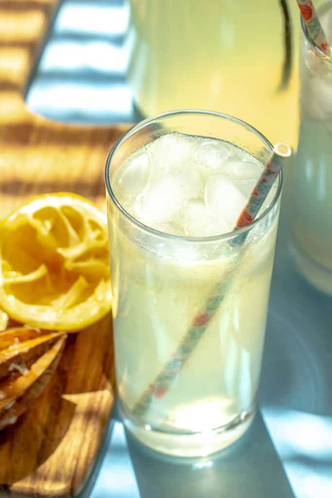glass of lemonade with paper straw in sunlight