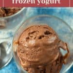 A clear glass bowl filled with creamy chocolate frozen yogurt sits on a blue fabric surface, inviting you to indulge in its rich, cool flavor.