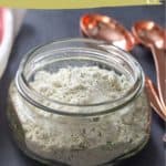 A glass jar filled with savory homemade ranch seasoning sits beside copper measuring spoons on a dark surface.