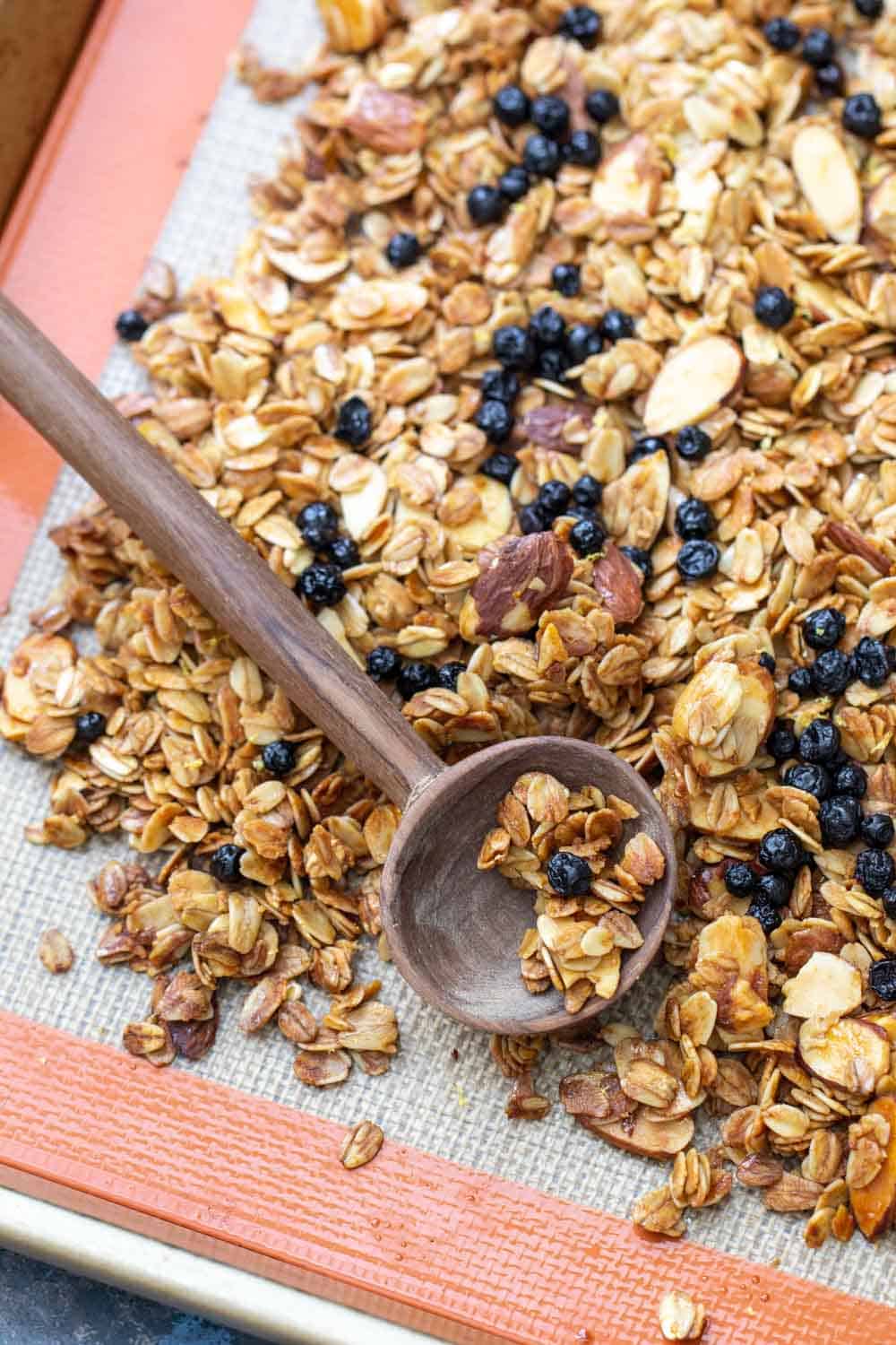 sheet pan of lemon blueberry granola with a wooden spoon