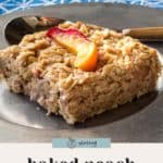 A square slice of baked peach oatmeal topped with a fresh peach slice is served on a plate with a fork.