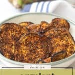 A bowl of seasoned, baked eggplant chips sits on a table, with a partial eggplant and kitchen towel in the background. Text overlay reads "eggplant chips." These crunchy eggplant chips make the perfect healthy snack.