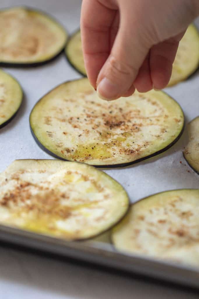 hand adding seasoning to eggplant slices