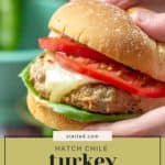 A hand holds a juicy hatch chile turkey burger stacked with lettuce, melted cheese, tomato slices, and a soft bun. The text overlay reads "Hatch Chile Turkey Burgers.