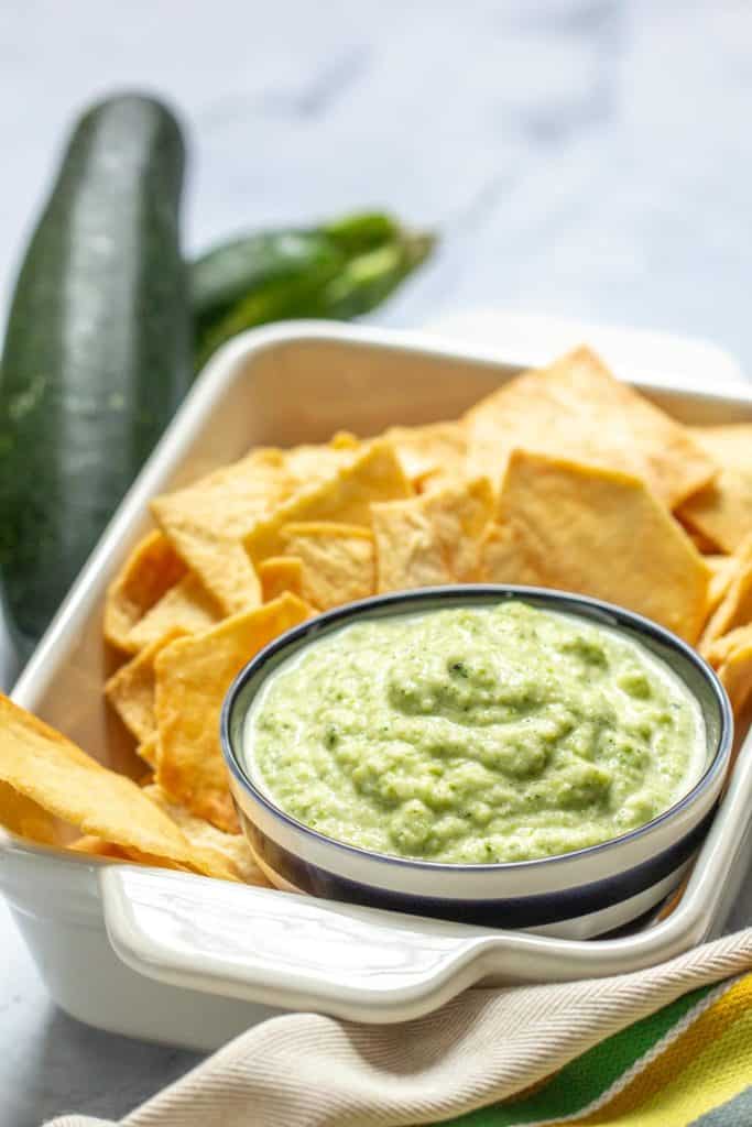 striped bowl of zucchini hummus served with pita chips