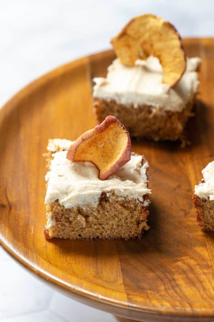 pieces of apple spice cake with brown butter frosting and apple chips on top