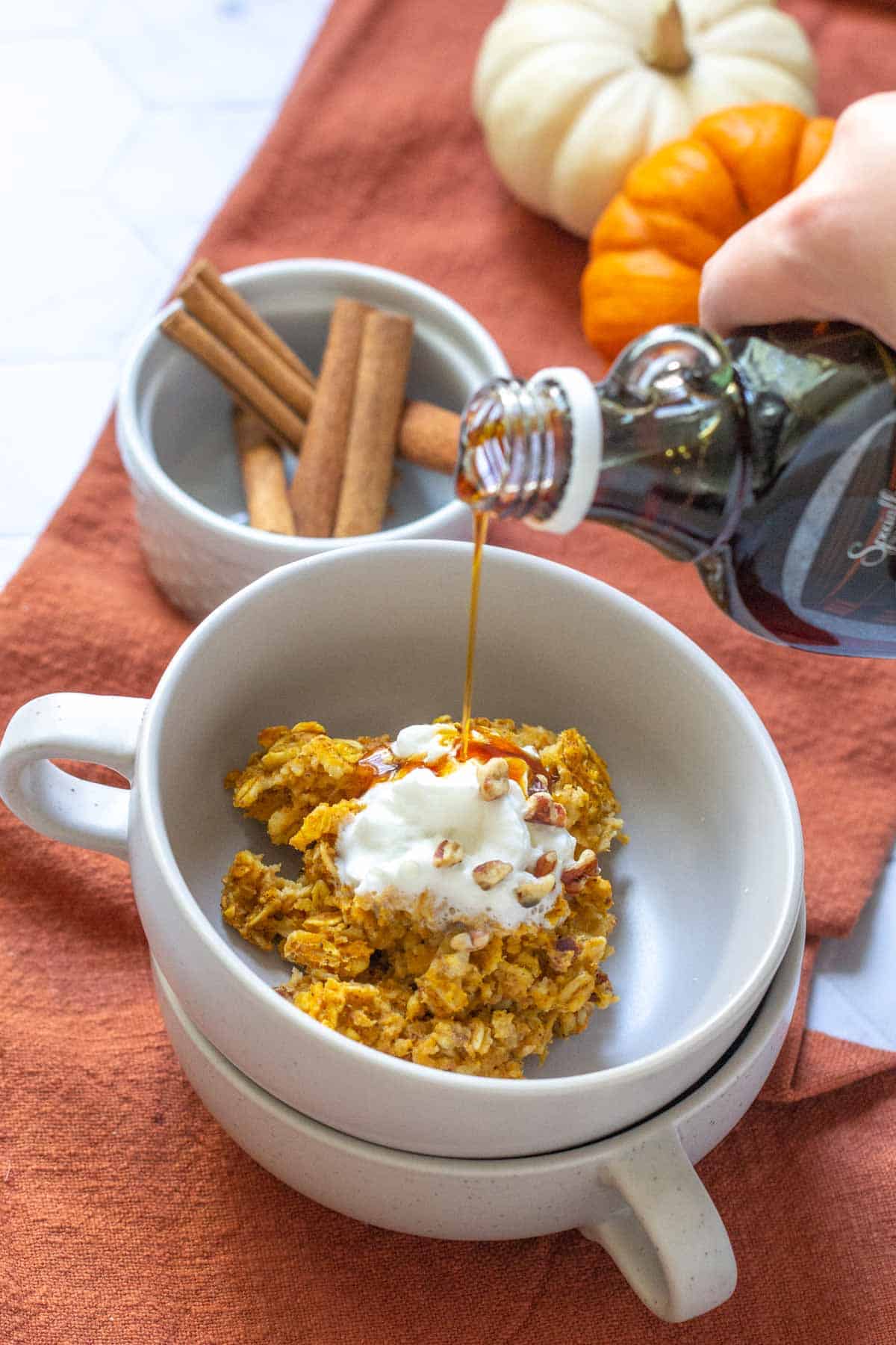 maple syrup being poured onto bowl of pumpkin baked oatmeal