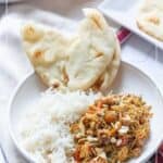 A bowl of white rice, slow cooker curried chicken, and two pieces of naan bread on a table, with additional plates visible in the background.