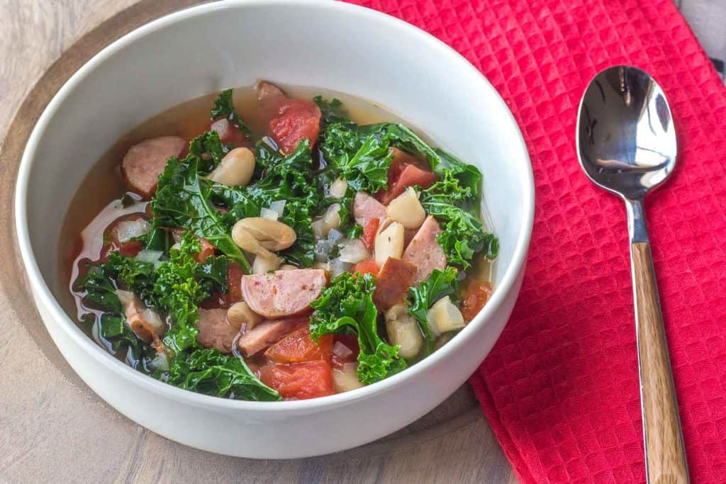 white bean sausage soup with kale in a white bowl